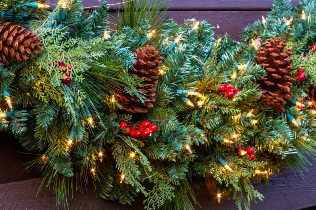 Lighted garland on brown vinyl fences with pine cones and red berries