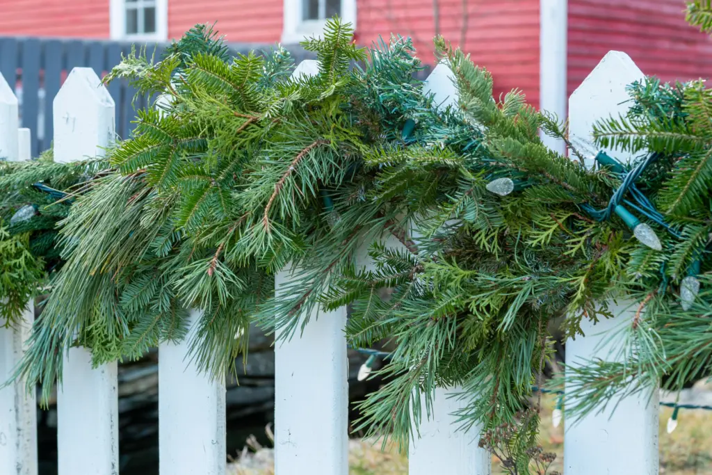 Pine branch fence decoration with lights on white fence