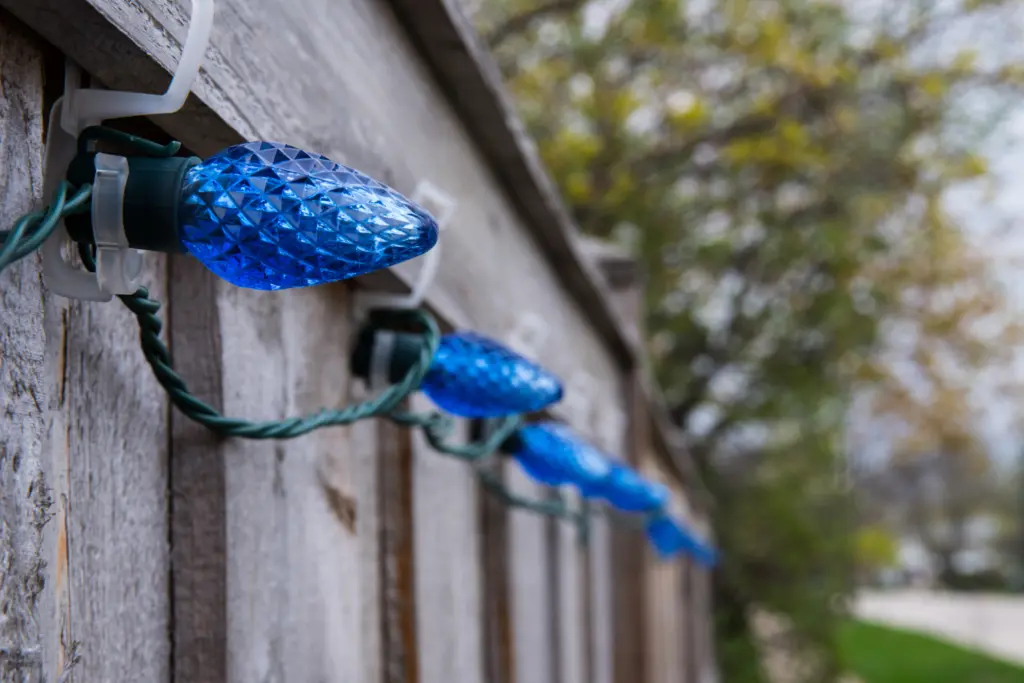 plastic self adhesive hooks holding blue acorn lights in place on fence