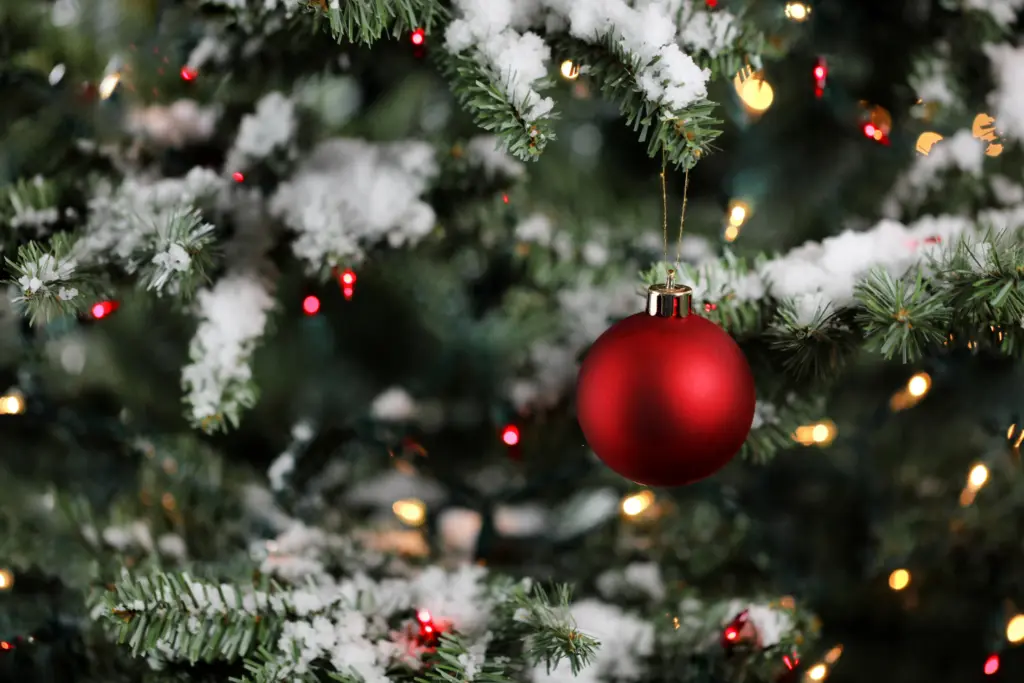 small red bauble christmas ornament on branch of artificial Christmas tree with white snow tips