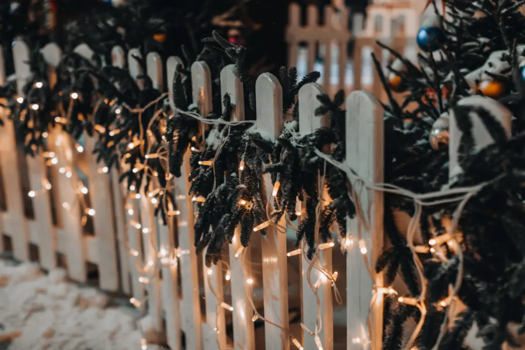 White icicle lights on a white picket fence with fir garland